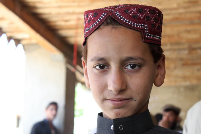 a boy in a turban looks into the camera while standing near a group of men