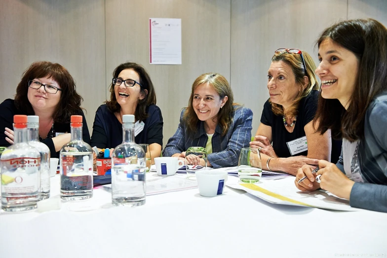 five women smiling at the camera as they sit around a table