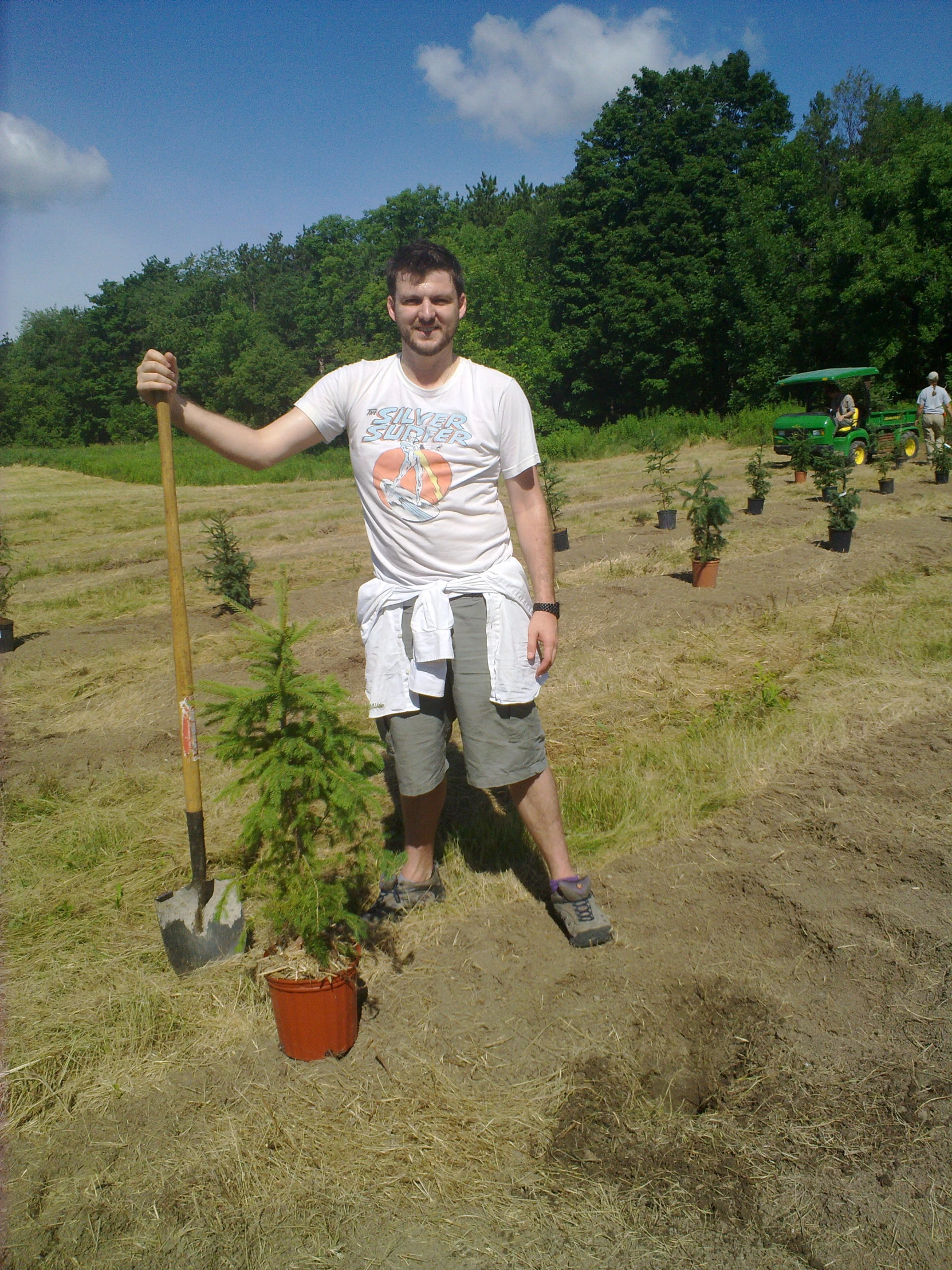 a man standing in a field holding a shovel and tree