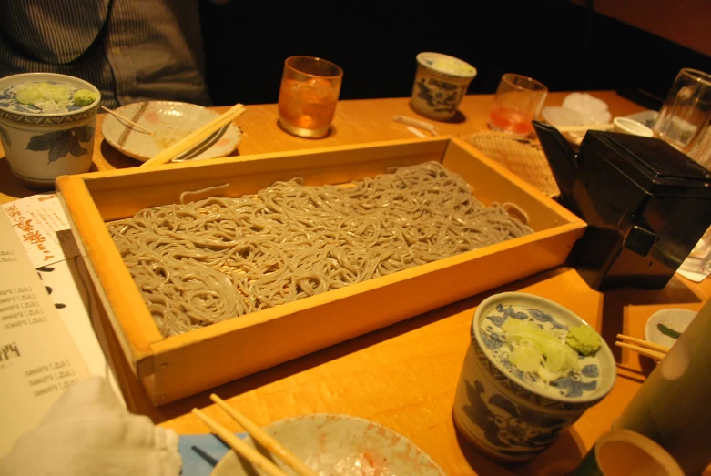 a tray of noodles on top of a table next to chopsticks and paper plates