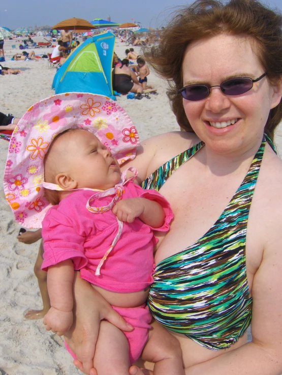 woman on a beach holding her baby with people in the background