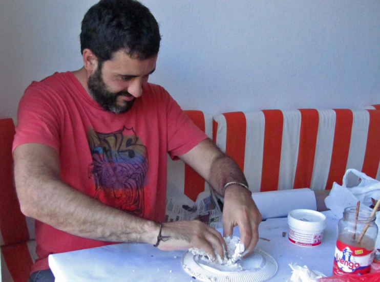 a man in red shirt using white cloth to decorate cake