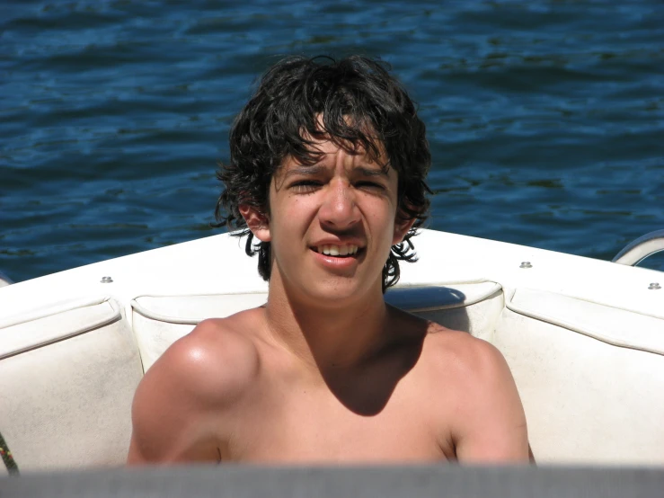 a shirtless boy on a white boat smiling