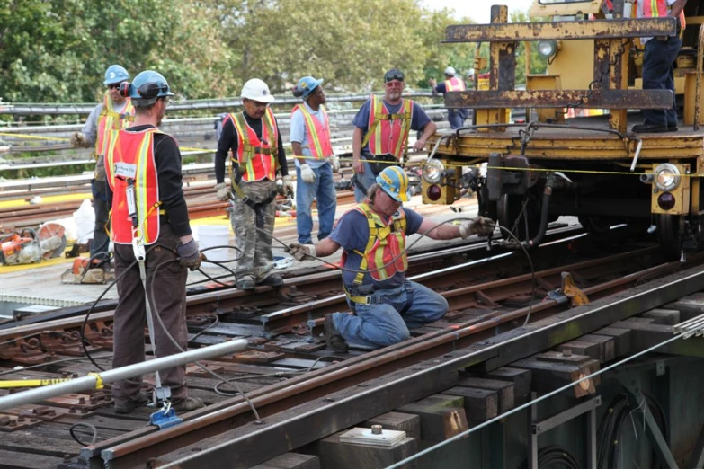 a group of workers stand on the side of train tracks