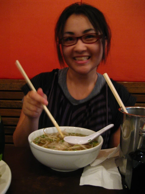 a woman sitting at a table with a bowl of soup and two chop sticks