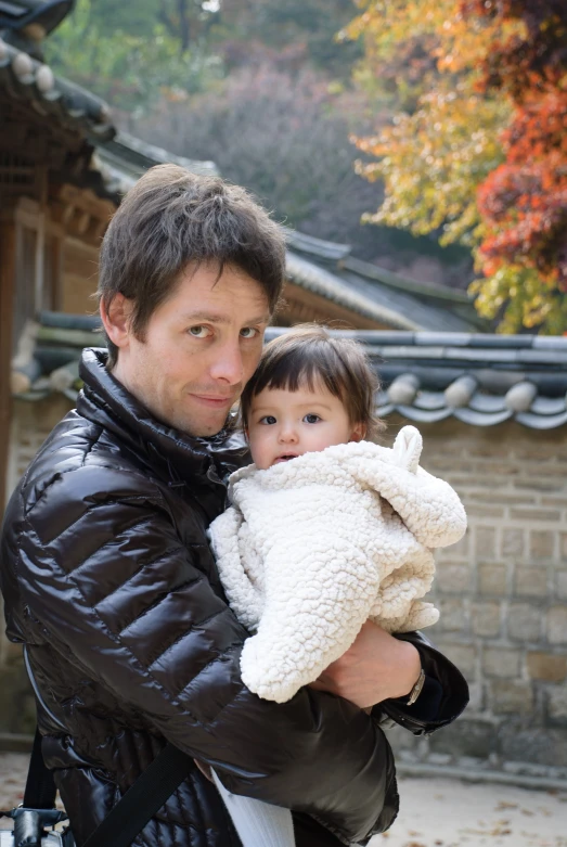 a man holding his young child outside in an autumn scene