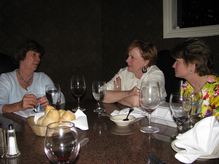 two woman and one man sitting at a table with wine glasses