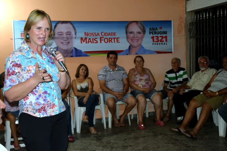 a woman stands in front of a group of people in front of a poster