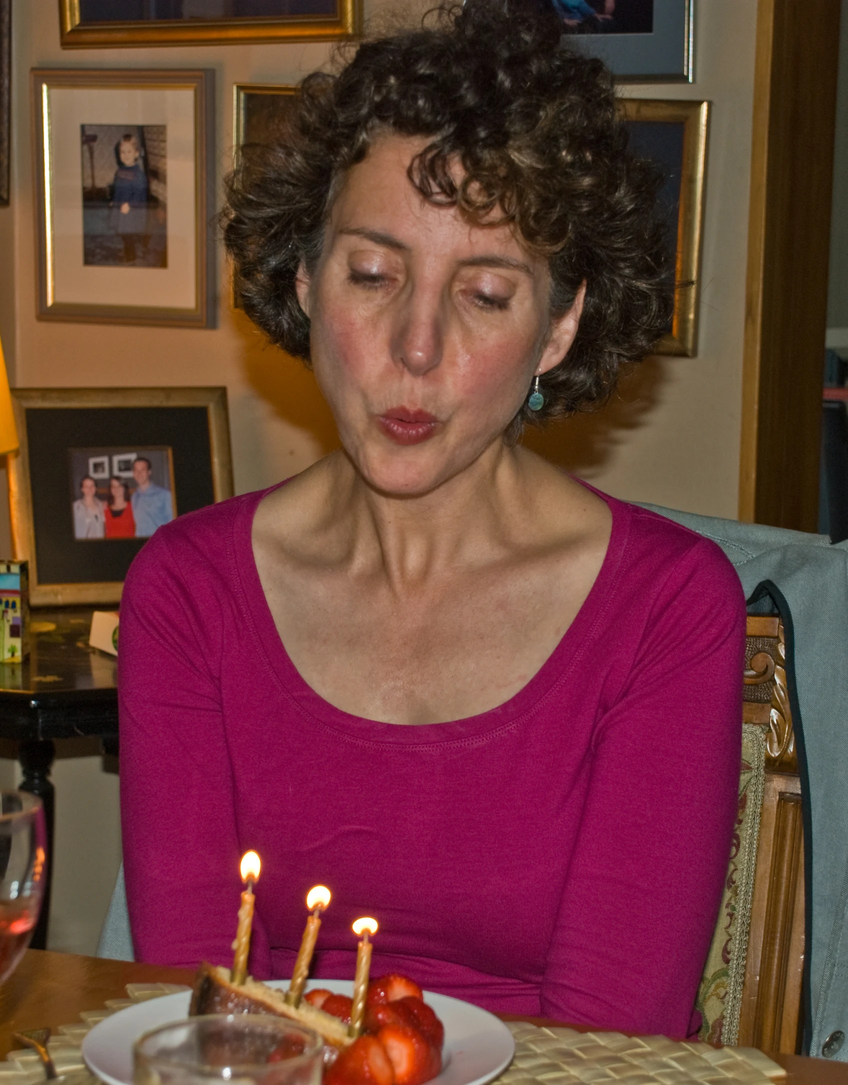 woman at table with three lit candles, looking at cake