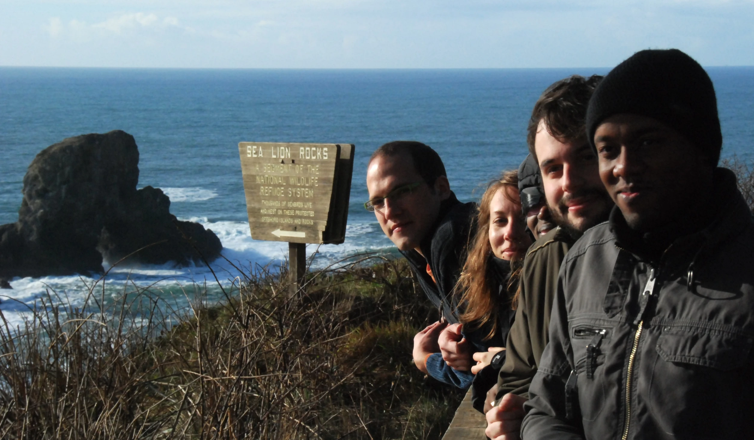 four people stand on the edge of a cliff overlooking the ocean