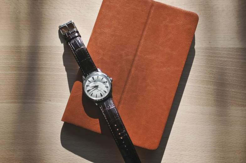 an orange journal and watch on a wooden table