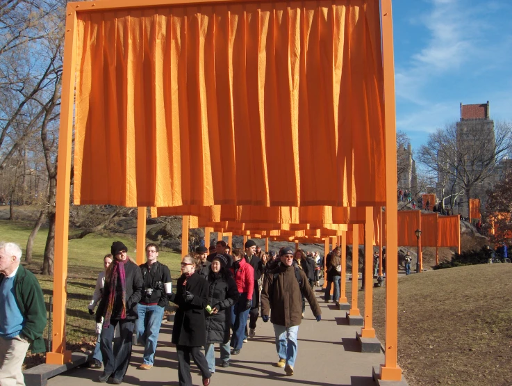 many people walking around near a large orange sculpture