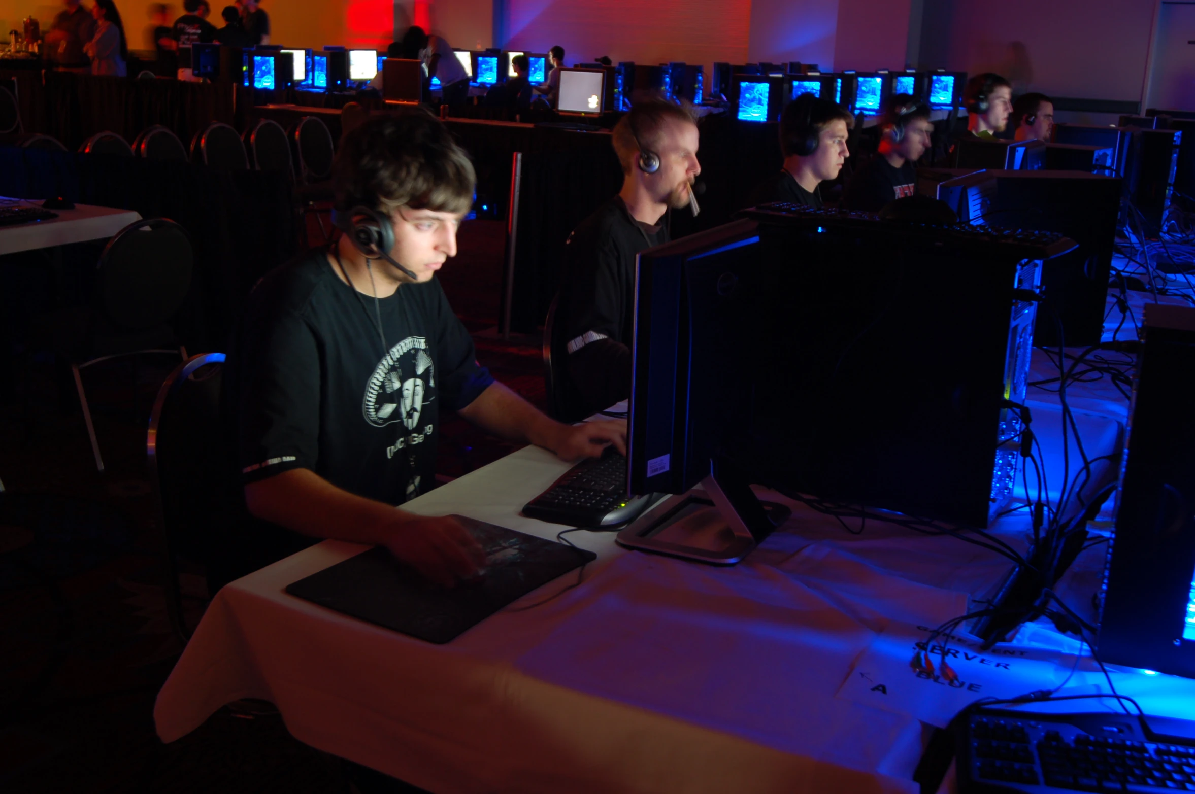 two guys sitting at computer monitors in a crowded room