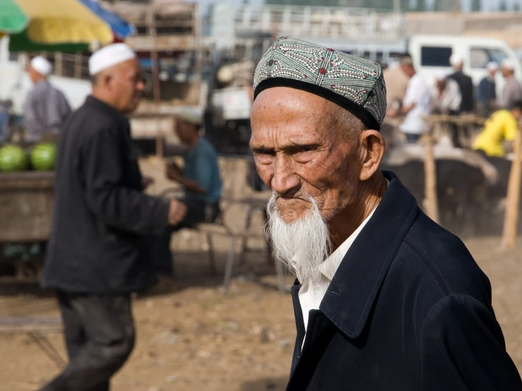 old man with long white hair and a beard on an outdoor market area