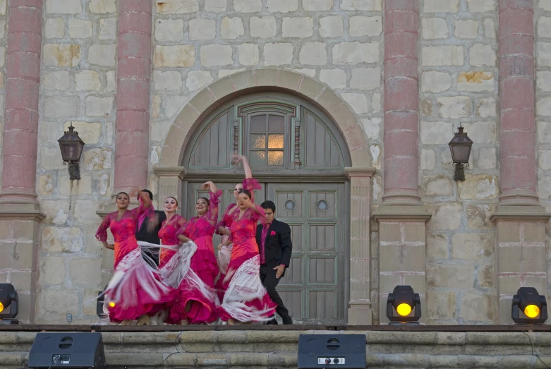 four women in long skirts, three wearing pink dresses and one wearing a blue suit and smiling