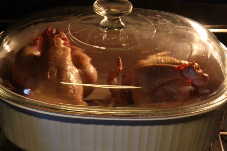 two chickens being cooked in a glass pot