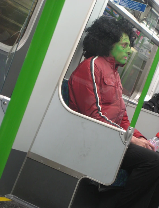 a man wearing a green mask sitting on a train