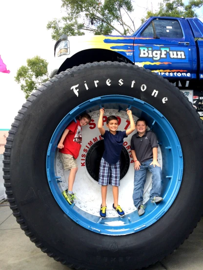 two boys standing on top of the tire of a truck