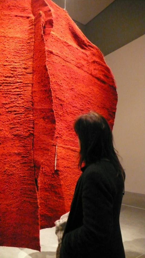 a woman looking at a red sculpture inside a museum