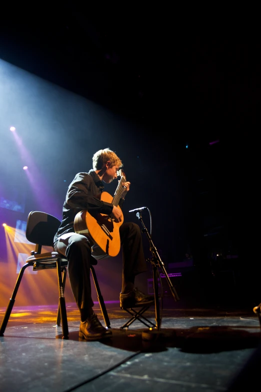 a man holding a guitar on top of a wooden chair