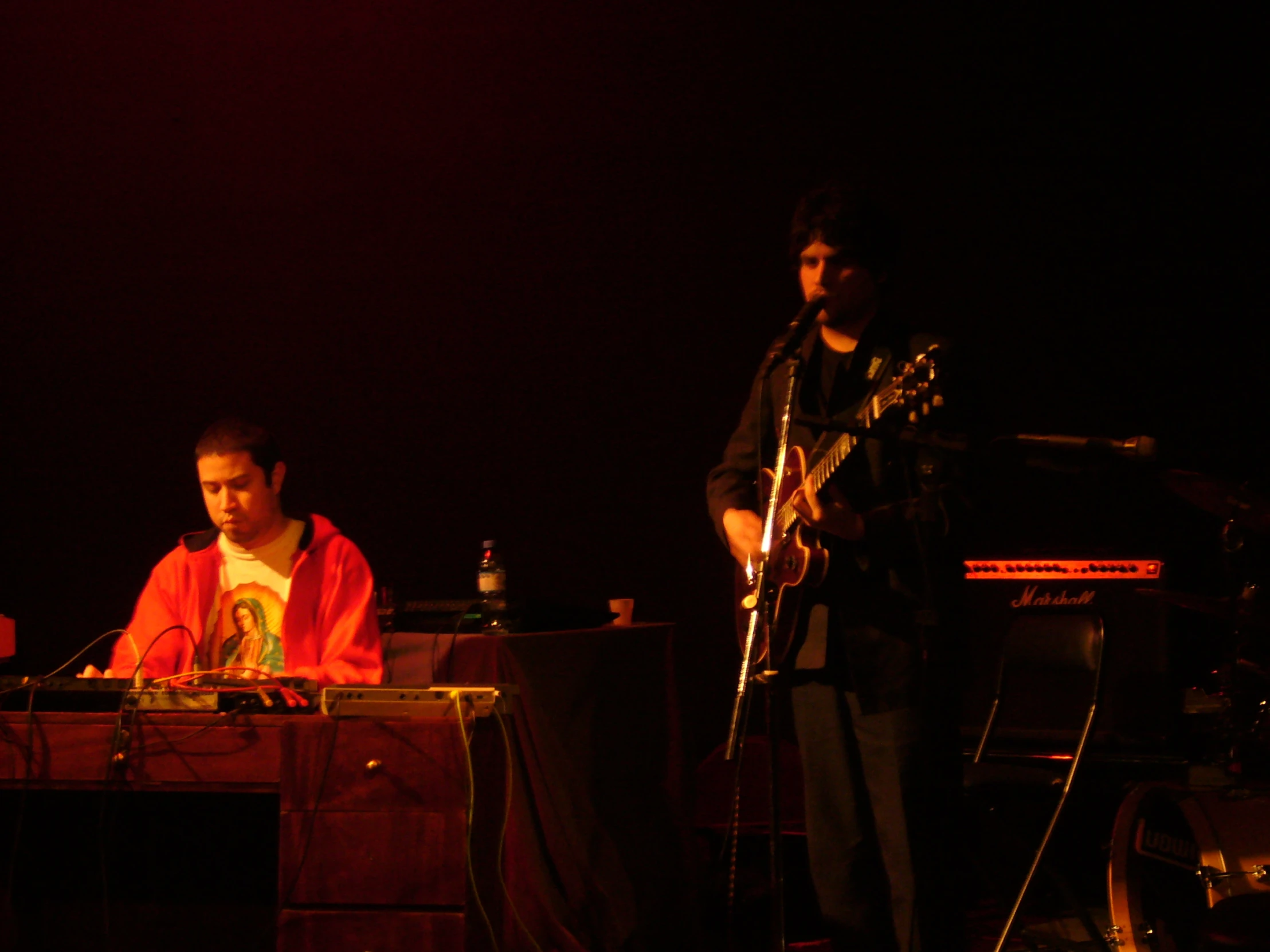 two men standing at a piano, one of them is playing a guitar