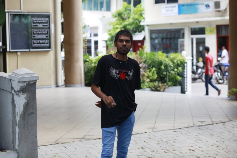 a man wearing a black shirt and jeans standing on a sidewalk