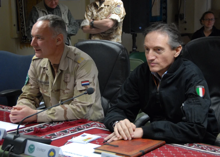 two men sitting at a table with a microphone in front of them