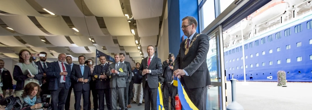 a group of people watching a man in suit stand behind a flag