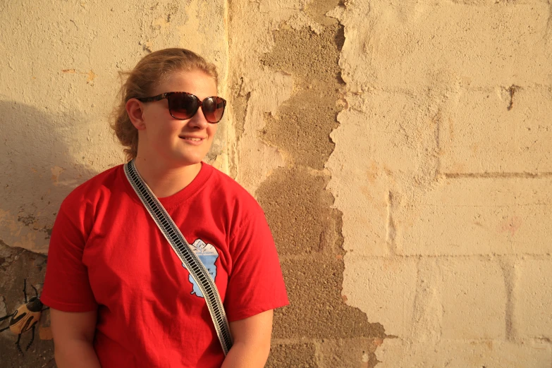 a person in sunglasses standing next to a stone wall