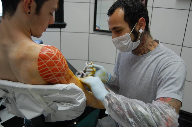 a man getting his chest tattoo tattooed by a tattooed doctor