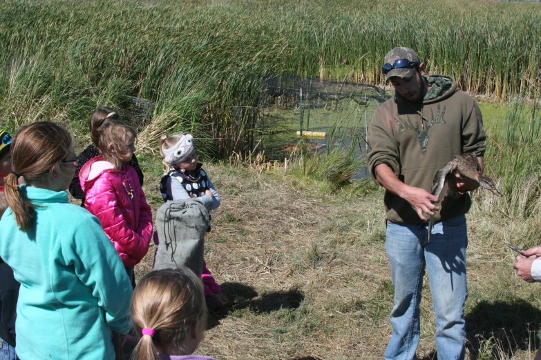 several children watching a man with a big chicken in his hand