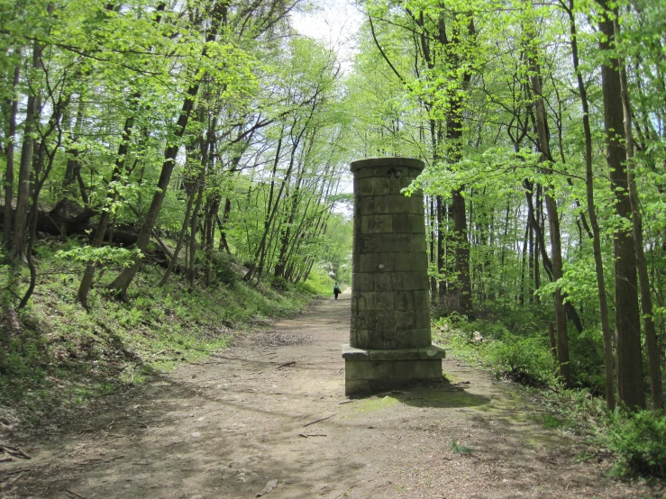 a path through a grassy area with a stone pillar surrounded by trees