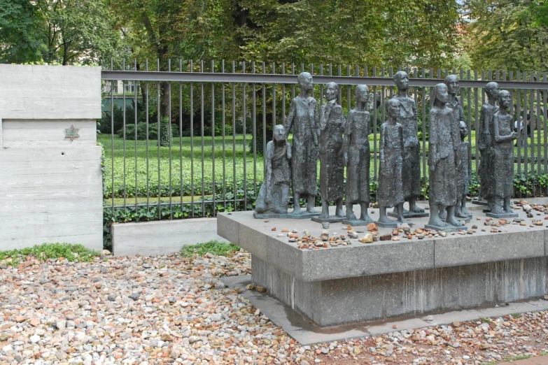 sculpture of men standing in front of fence with trees in background