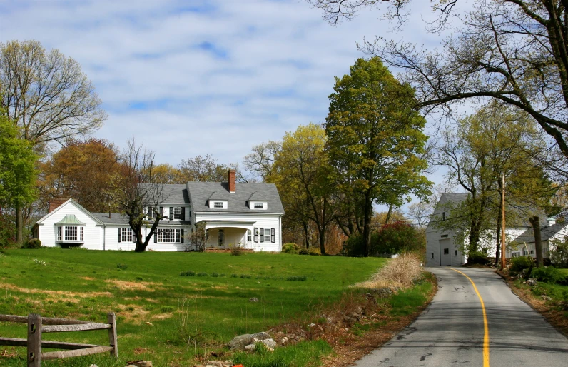 a country road leading to a large white house in the woods