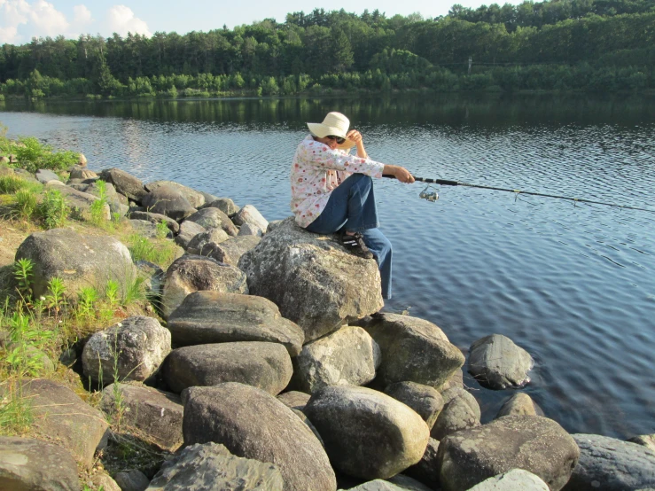 a man fishing in the water from rocks on the side of a lake