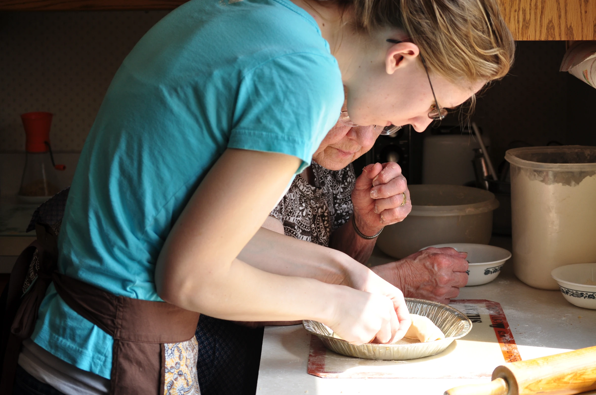 the women in a kitchen are working together on the pizza