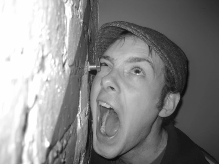 a man standing against a brick wall opening his mouth