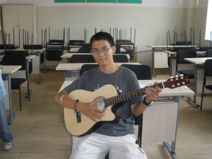 there is a man sitting in front of a desk playing guitar