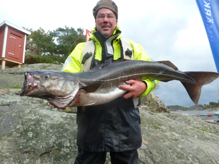 a man in yellow jacket holding up a large fish