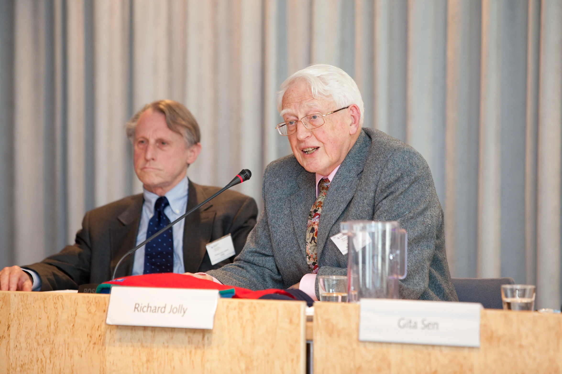 a man and a woman sit at a table while a man speaks into a microphone