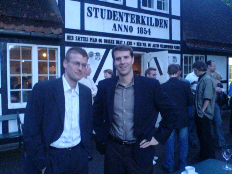 two men standing next to each other in front of a building