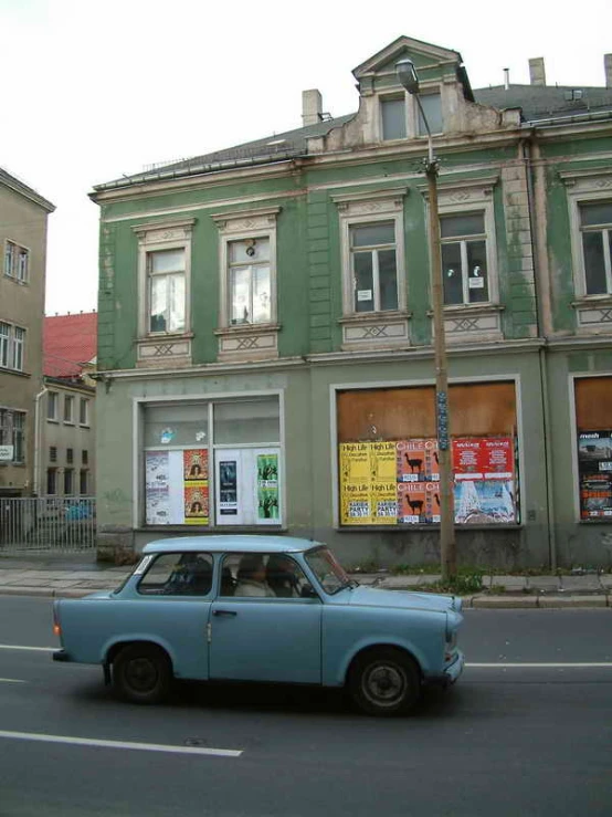 a small blue car driving past a tall building