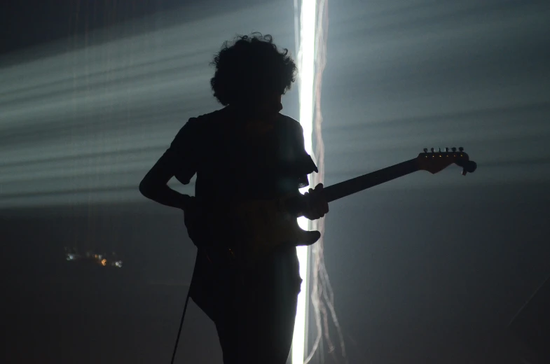 a silhouette of a guitar player holding a guitar against a background of rays