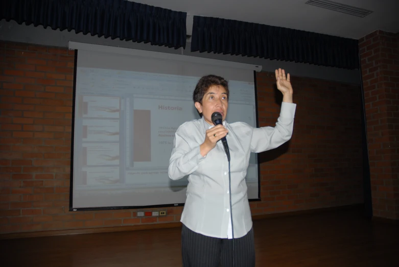 woman speaking into microphone on stage with projection screen in background