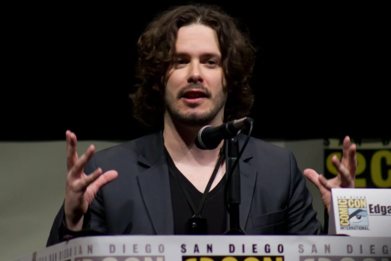 a man talking on stage in front of a microphone