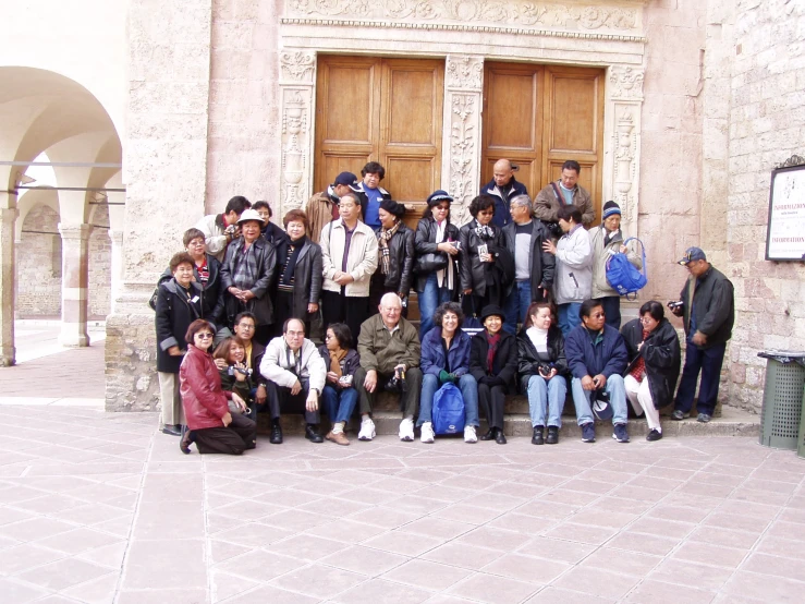 a group of people sit and pose outside an old style building