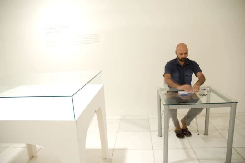 a man sitting at a desk in front of a white wall