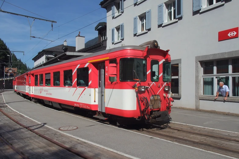 a red and white passenger train on tracks next to buildings