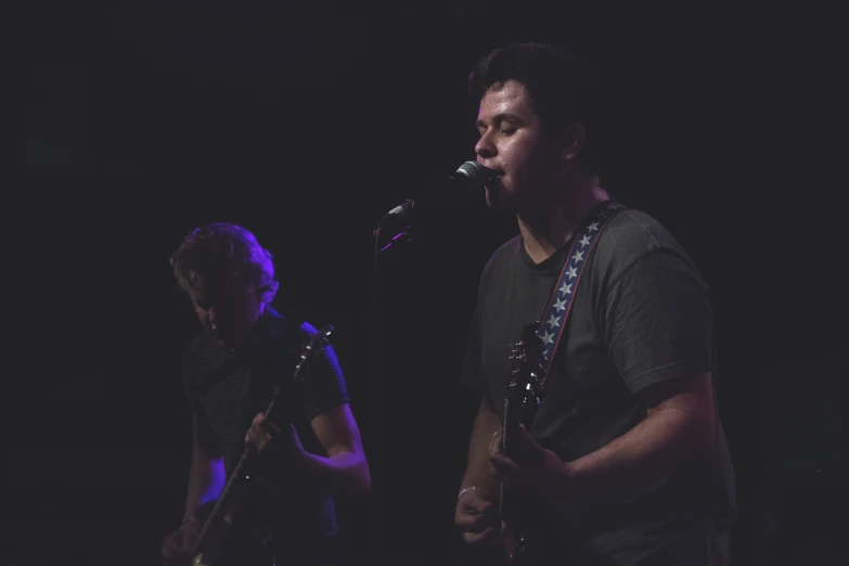 two people playing guitar on stage with purple lighting