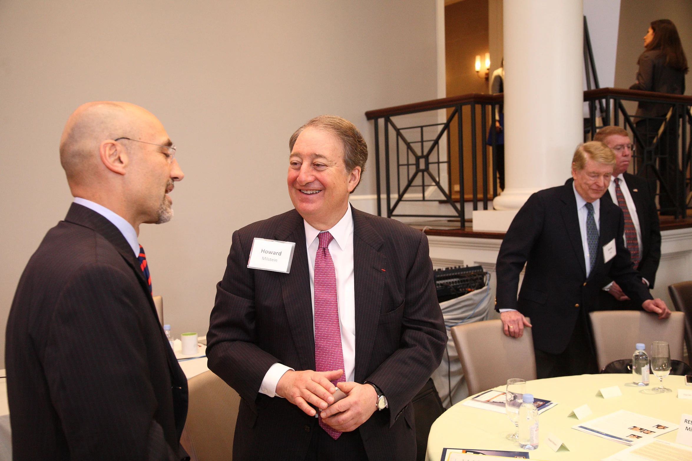 two men stand talking to each other at a meeting